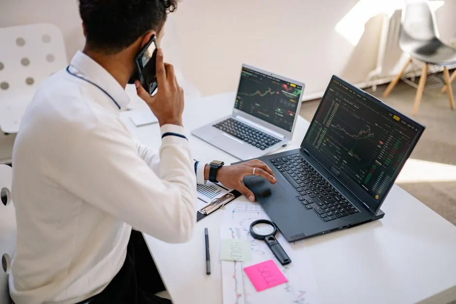 Man working on multiple laptops with financial charts visible on screens at a desk